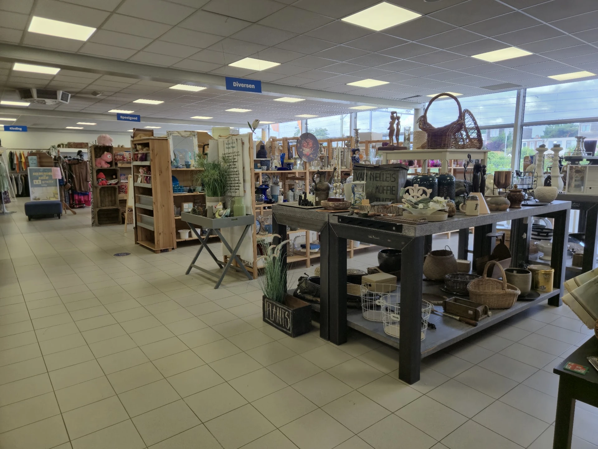 Winkelvloer van een kringloopwinkel met stellingen, toonbanken en diverse tweedehandsartikelen zoals meubels, huishoudspullen
