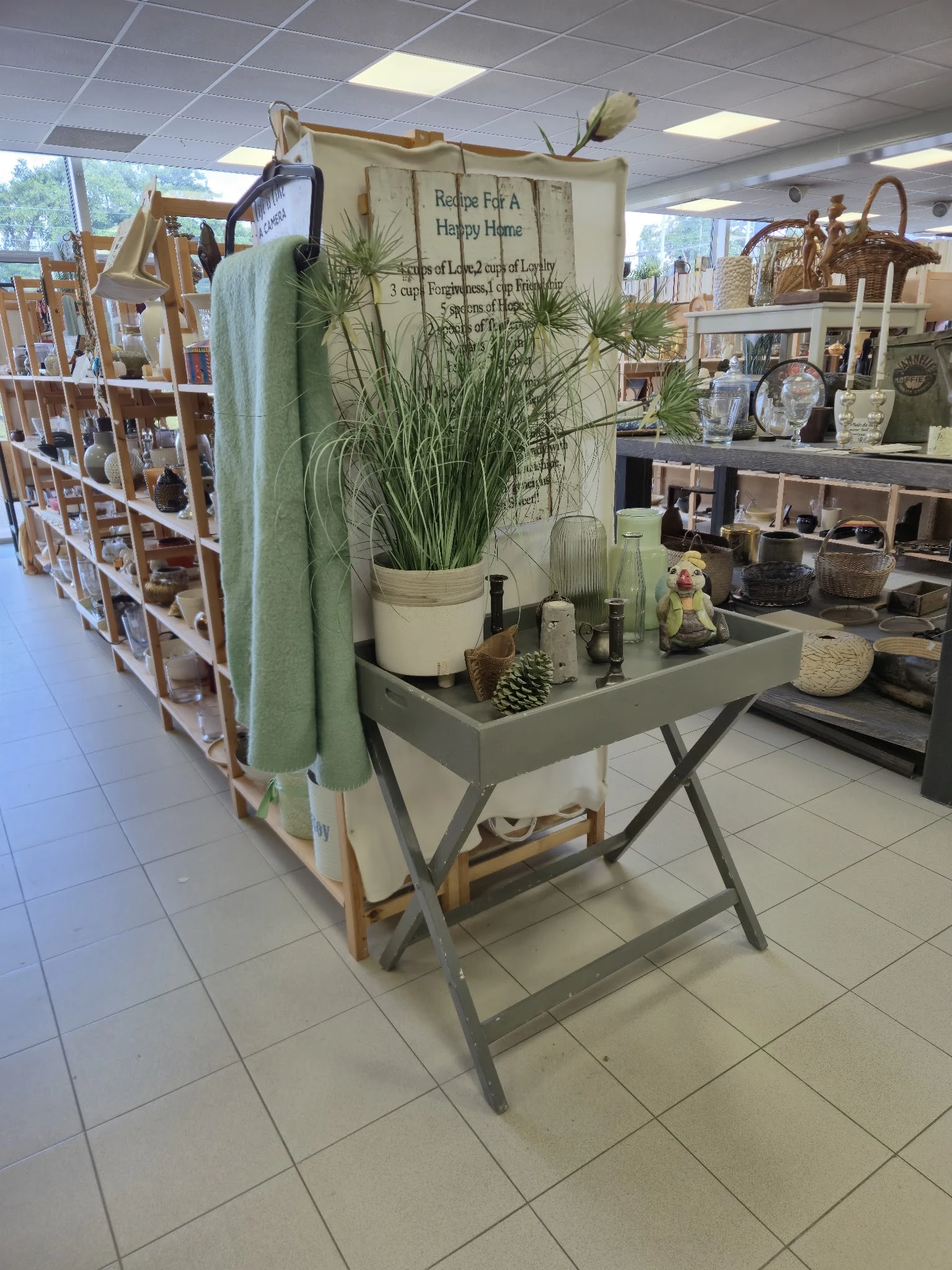Grijze tafel met plantenpot, decoratieve items en huishoudartikelen in een kringloopwinkel
