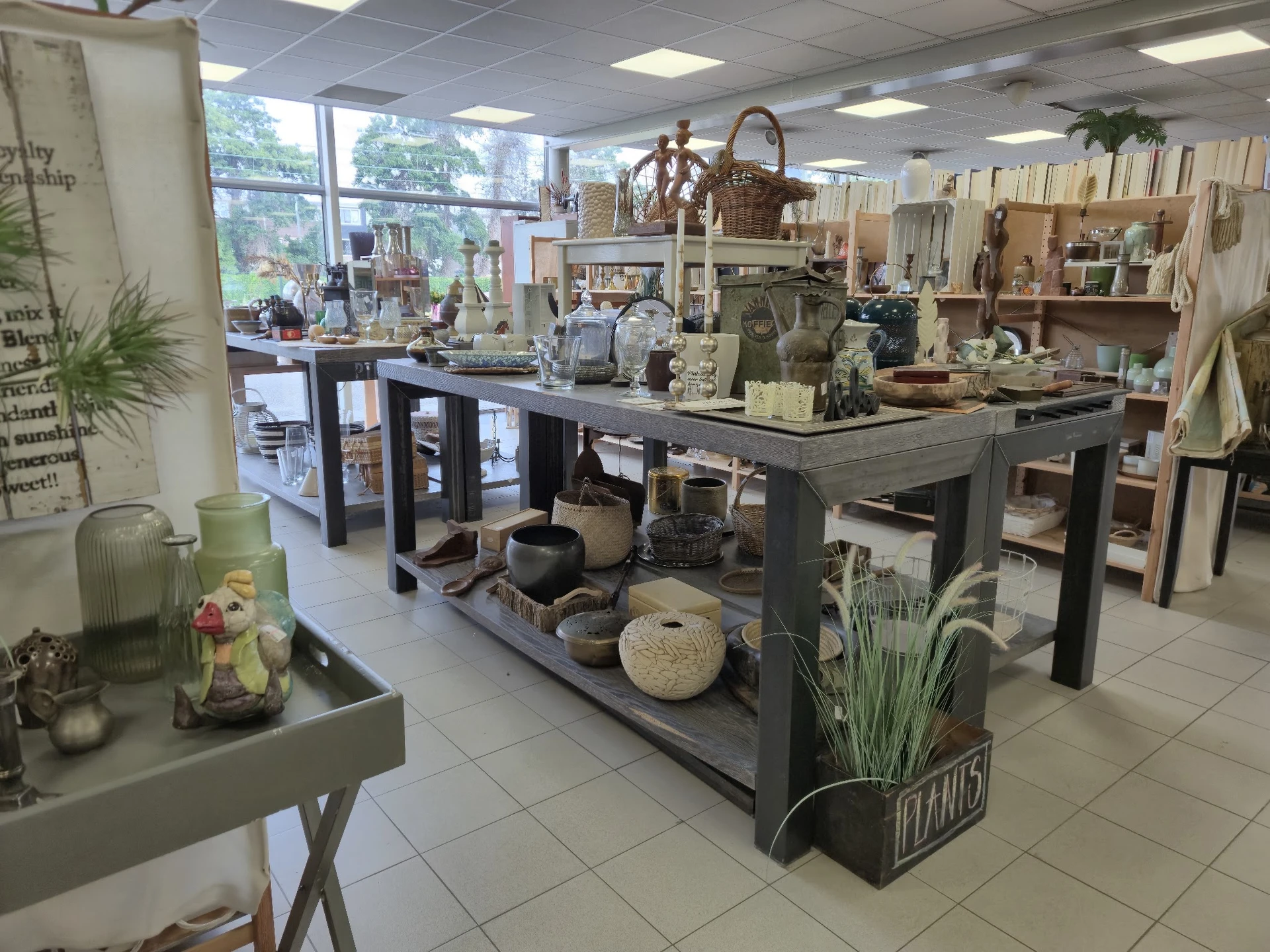 Winkelvloer van kringloopwinkel met tafels vol huishoudelijke artikelen, decoratie en meubelstukken