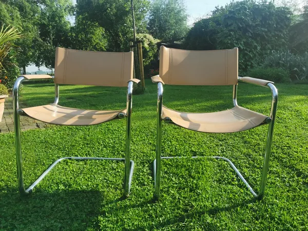 Twee beige en zilverkleurige designstoelen met armleuningen op een grasveld