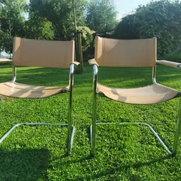 Twee beige en zilverkleurige designstoelen met armleuningen op een grasveld