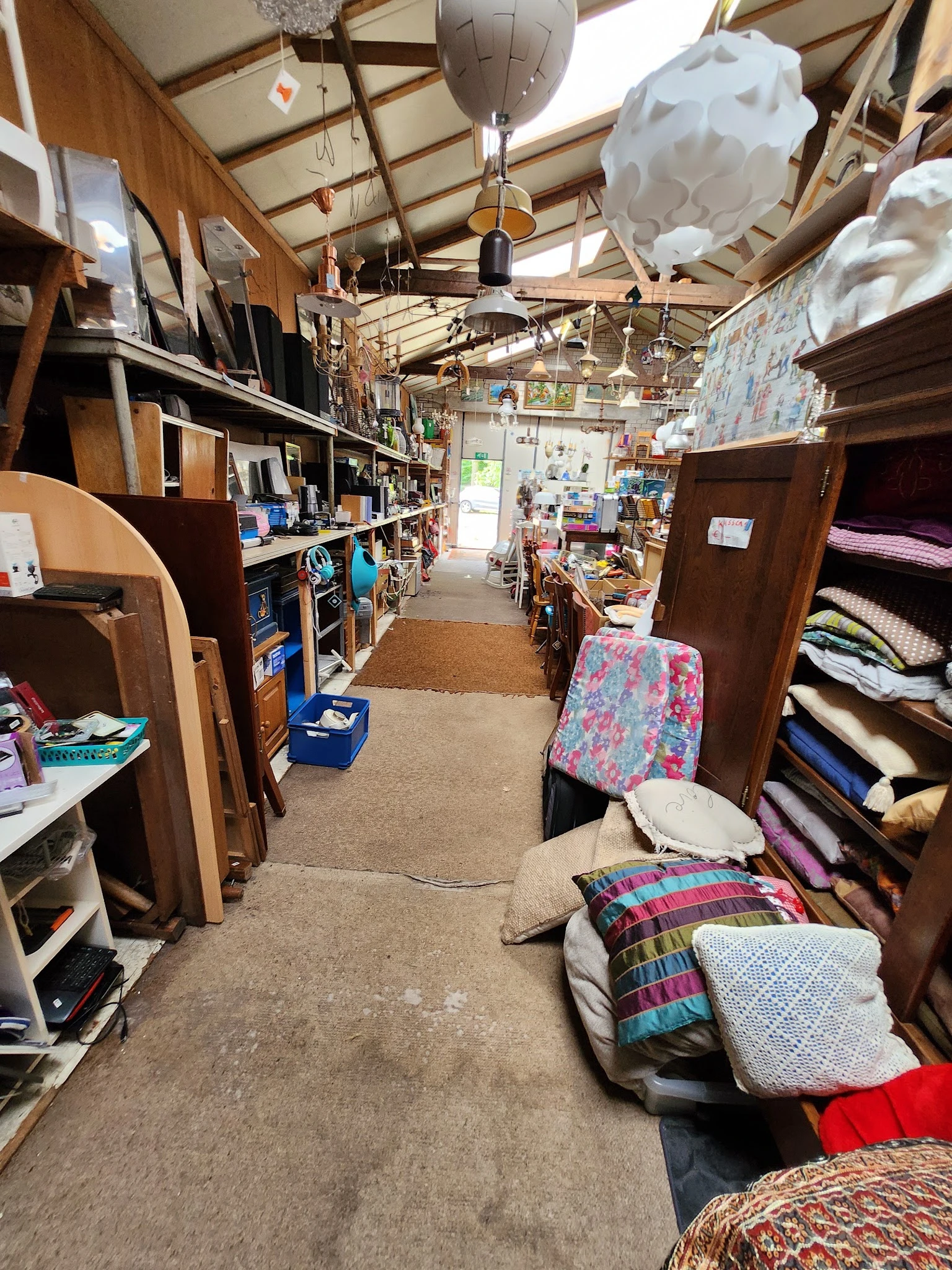 Winkelvloer van kringloopwinkel met houten meubels, textiel en huishoudelijke artikelen langs de zijkanten