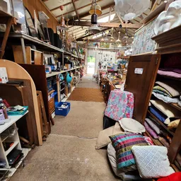 Winkelvloer van kringloopwinkel met houten meubels, textiel en huishoudelijke artikelen langs de zijkanten
