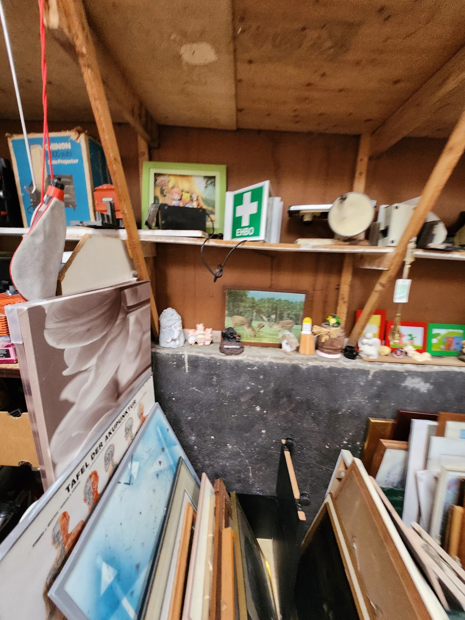 Schappen en werkblad in kringloopwinkel met diverse gebruikte voorwerpen, eerste hulpkist en afbeeldingen aan de muur