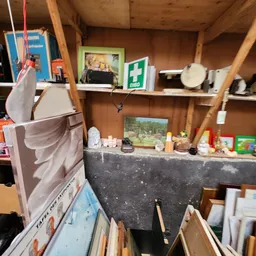 Schappen en werkblad in kringloopwinkel met diverse gebruikte voorwerpen, eerste hulpkist en afbeeldingen aan de muur