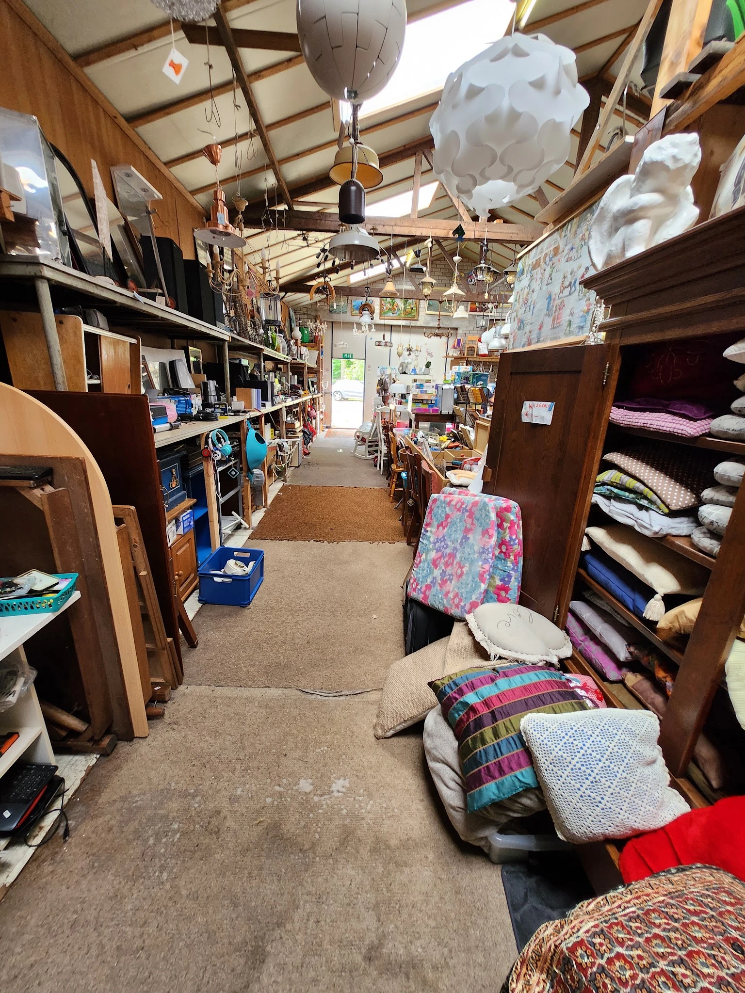 Winkelinterieur met houten kasten, stellingen met diverse spullen, beddelinnen en textiel langs de wanden