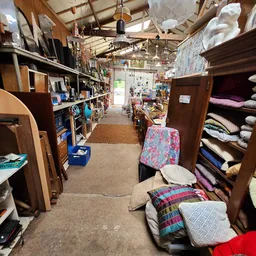 Winkelinterieur met houten kasten, stellingen met diverse spullen, beddelinnen en textiel langs de wanden