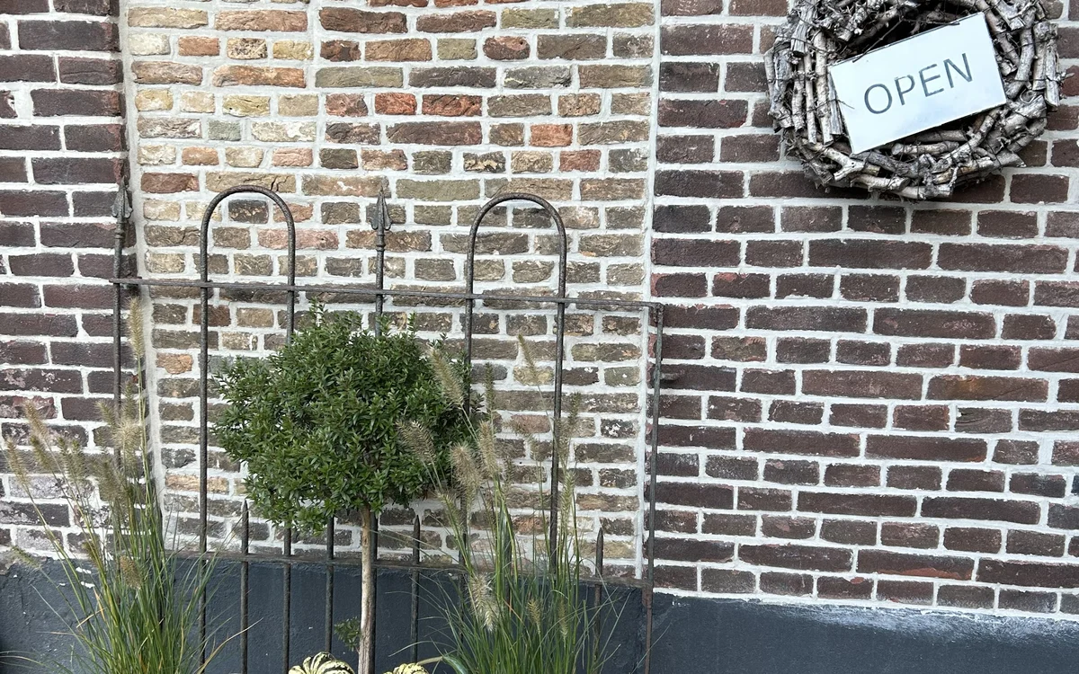 Bakstenen gevel met open kranz, metalen plantenbak en 'OPEN'-bord