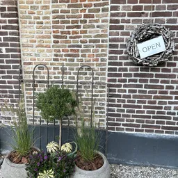 Bakstenen gevel met open kranz, metalen plantenbak en 'OPEN'-bord
